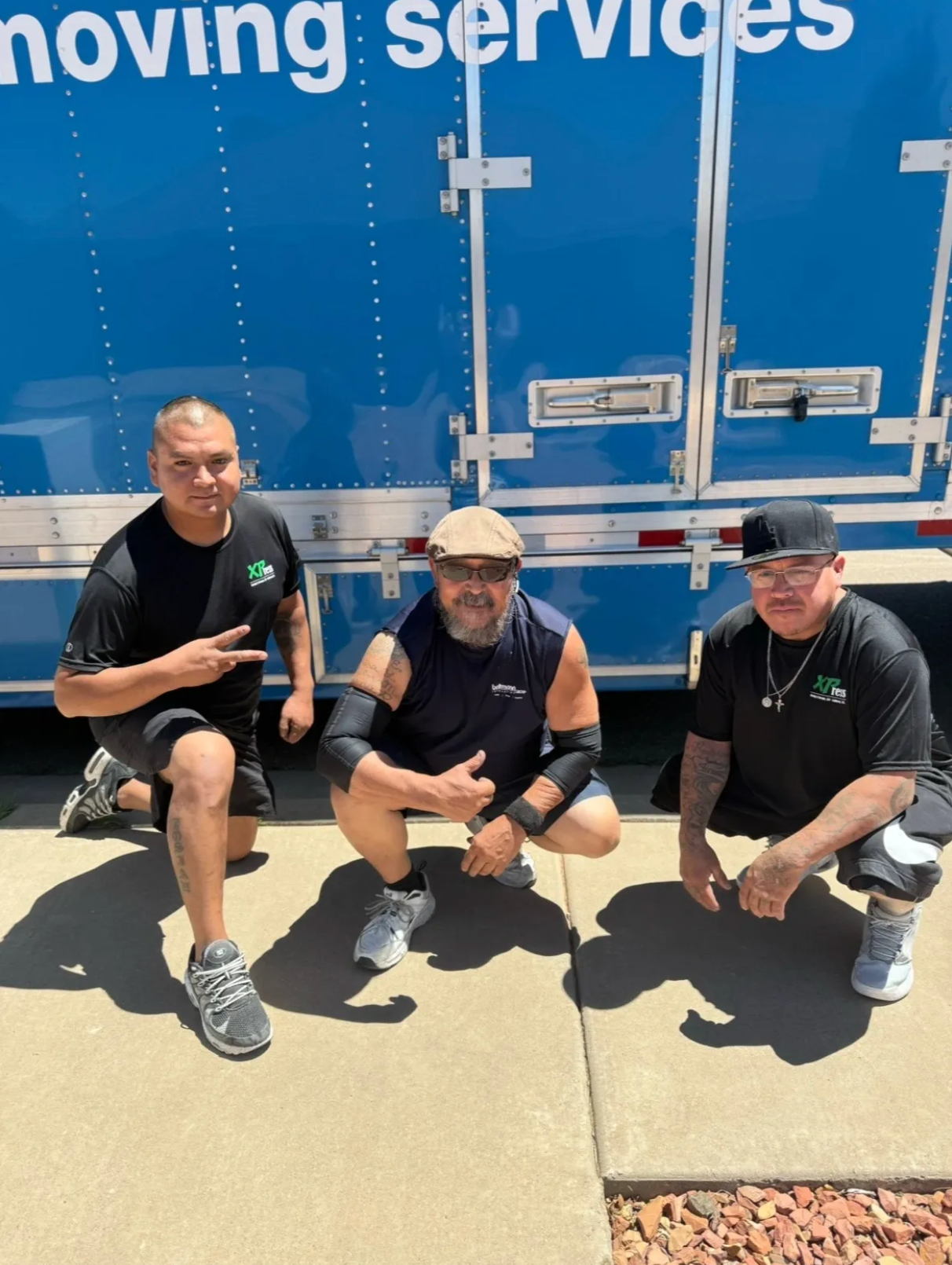 Three men are posing for a picture in front of a moving service truck