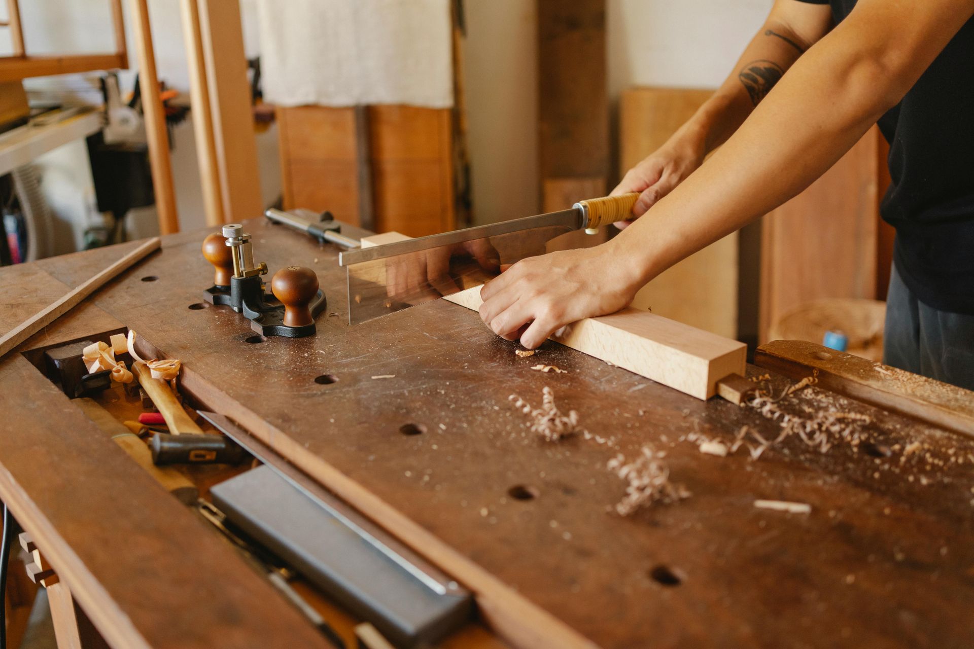 Person sawing wood with a hand saw at a workbench in a workshop.
