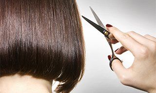 A pair of scissors being held up next to a short black bob hairsytyle