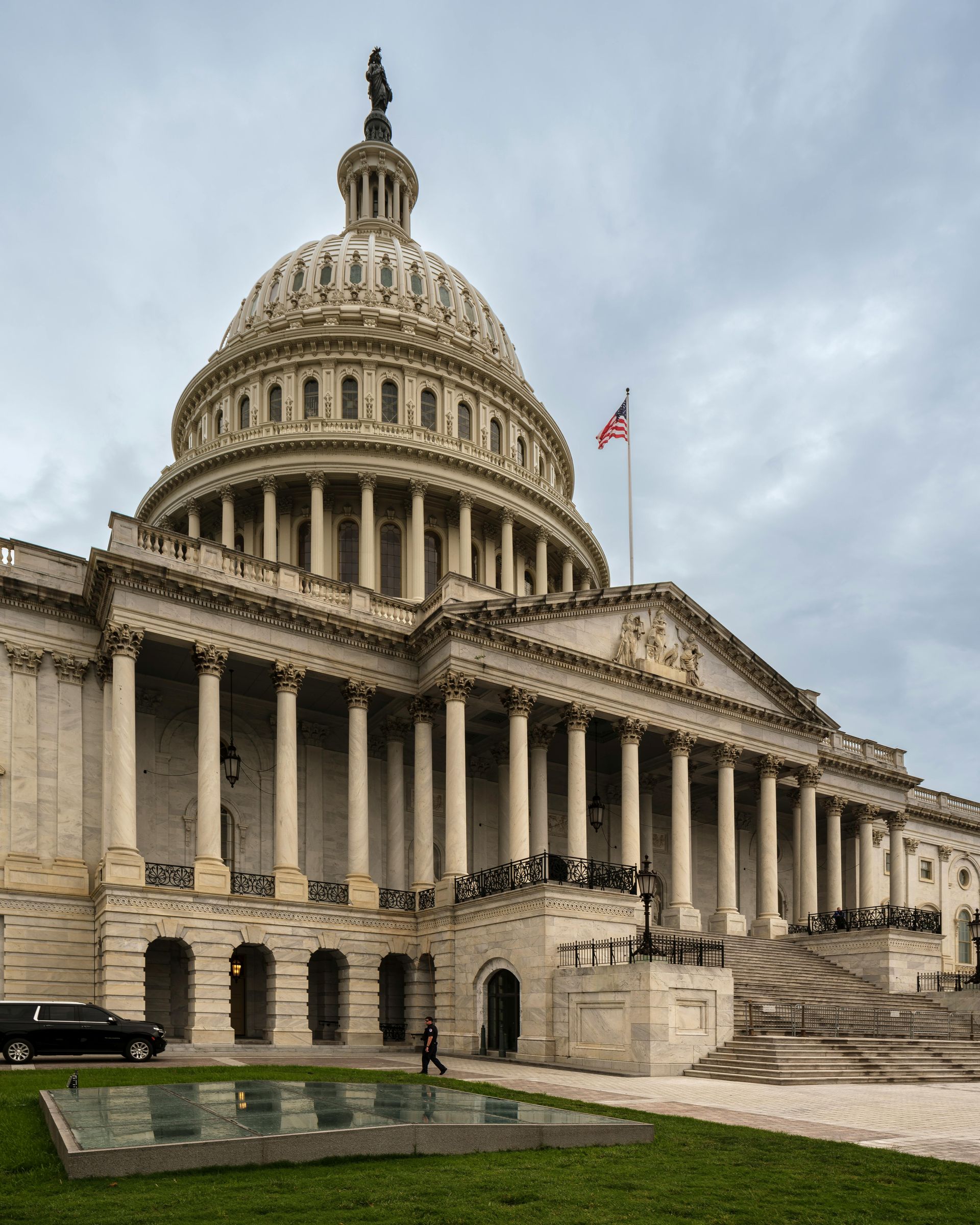 U.S. Capitol Building in Washington, D.C., with its iconic dome, columns, and American flag under cloudy skies.