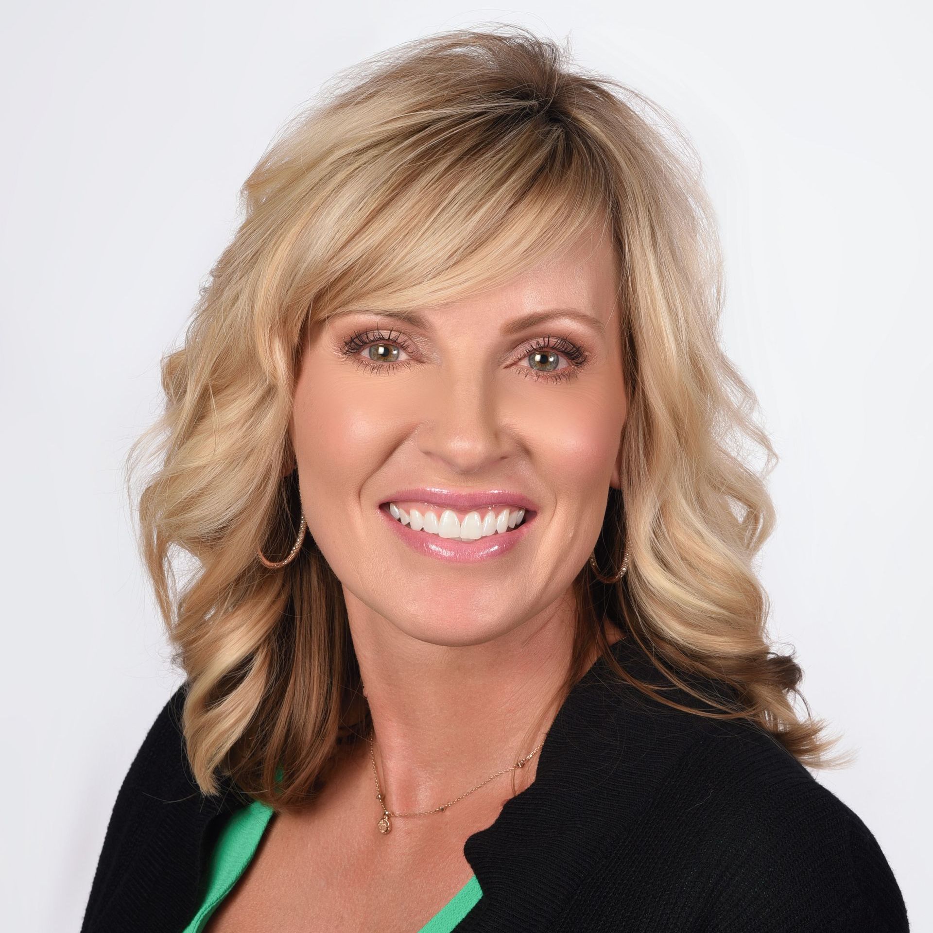 A woman wearing a black jacket and a green shirt is smiling for the camera.
