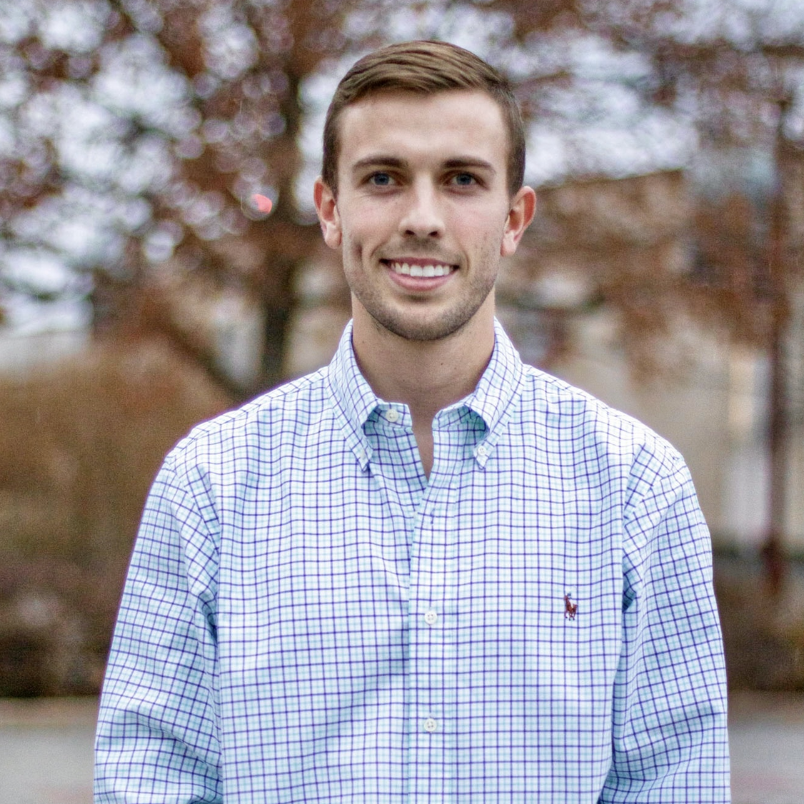 A man in a blue and white plaid shirt is smiling for the camera.