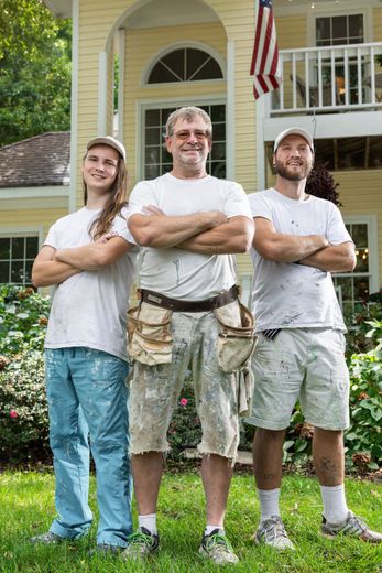 Three men are standing in front of a house with their arms crossed.