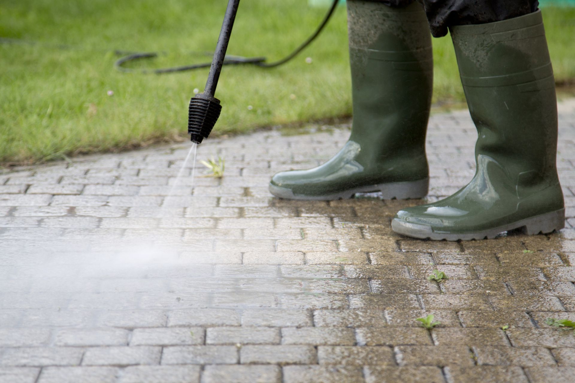 A person is using a high pressure washer to clean a brick walkway.