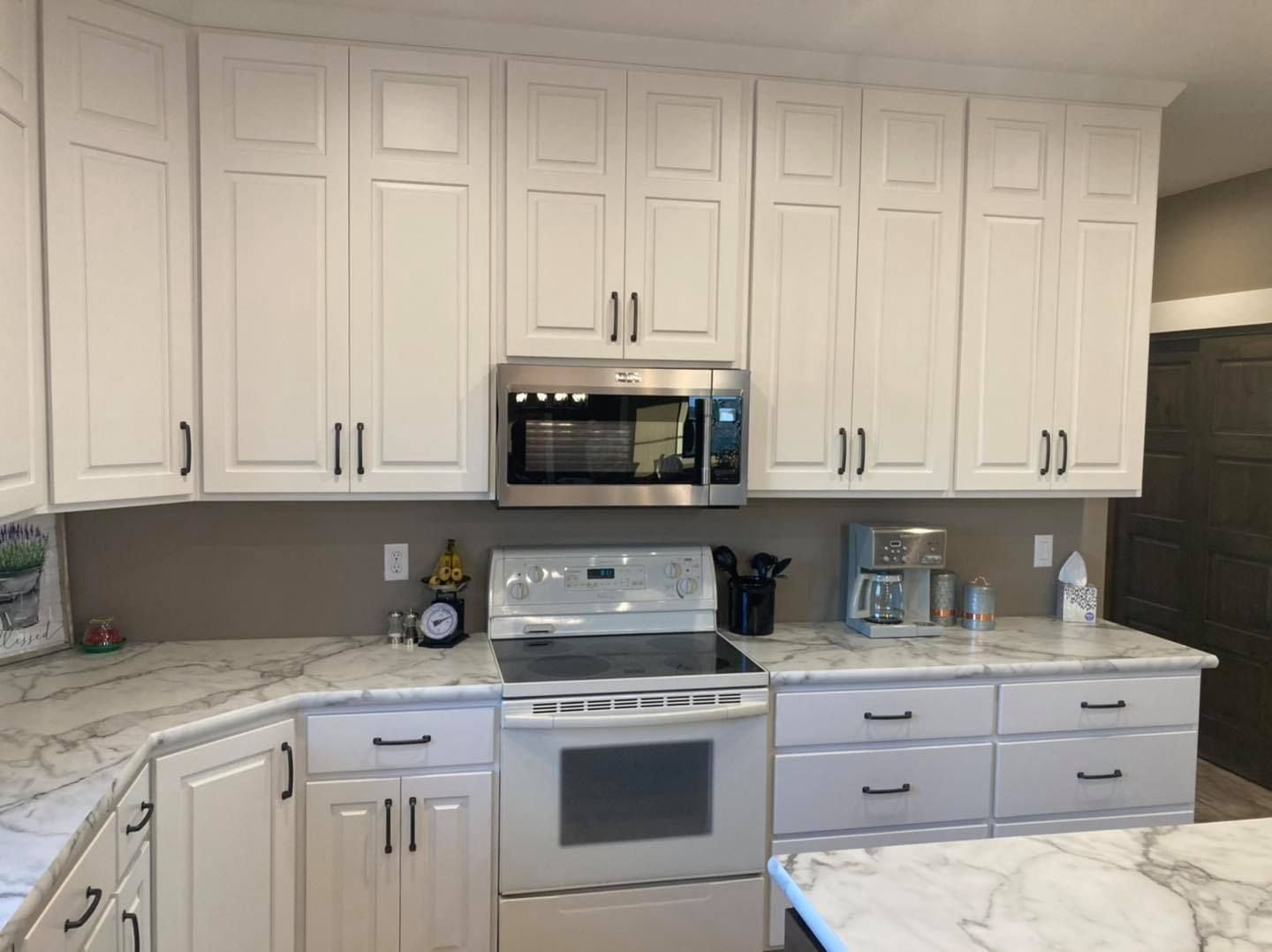 A kitchen with white cabinets , a stove , a microwave , and a coffee maker.
