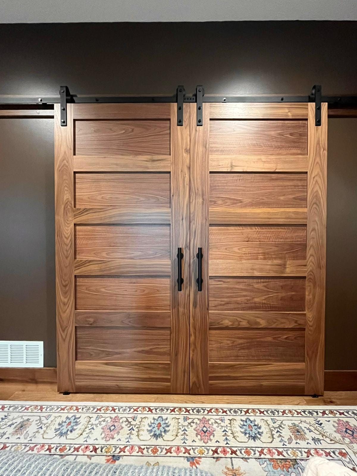 A pair of wooden sliding barn doors in a room with a rug.
