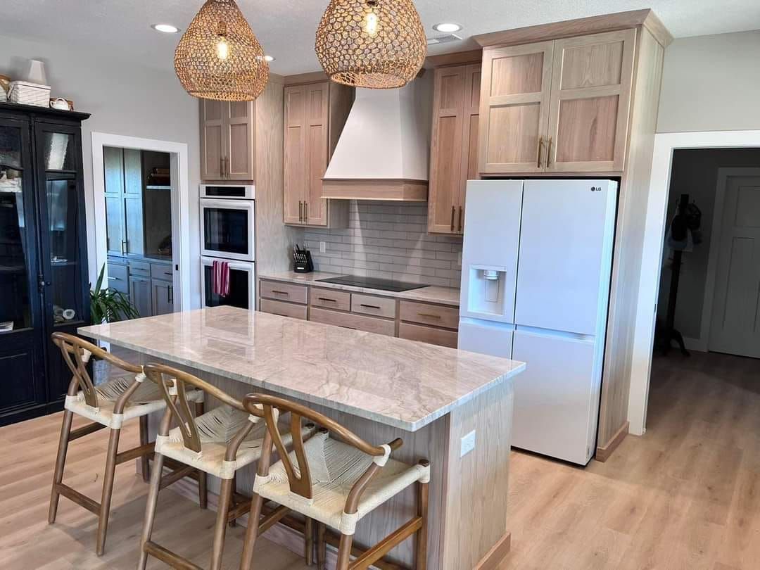 A kitchen with a large island , stools and a refrigerator.