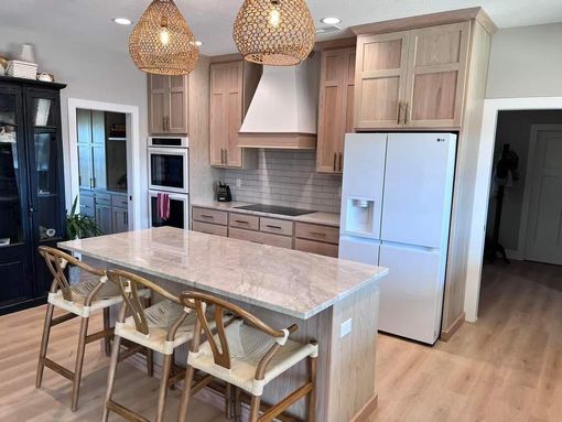 A kitchen with a large island , stools and a refrigerator.
