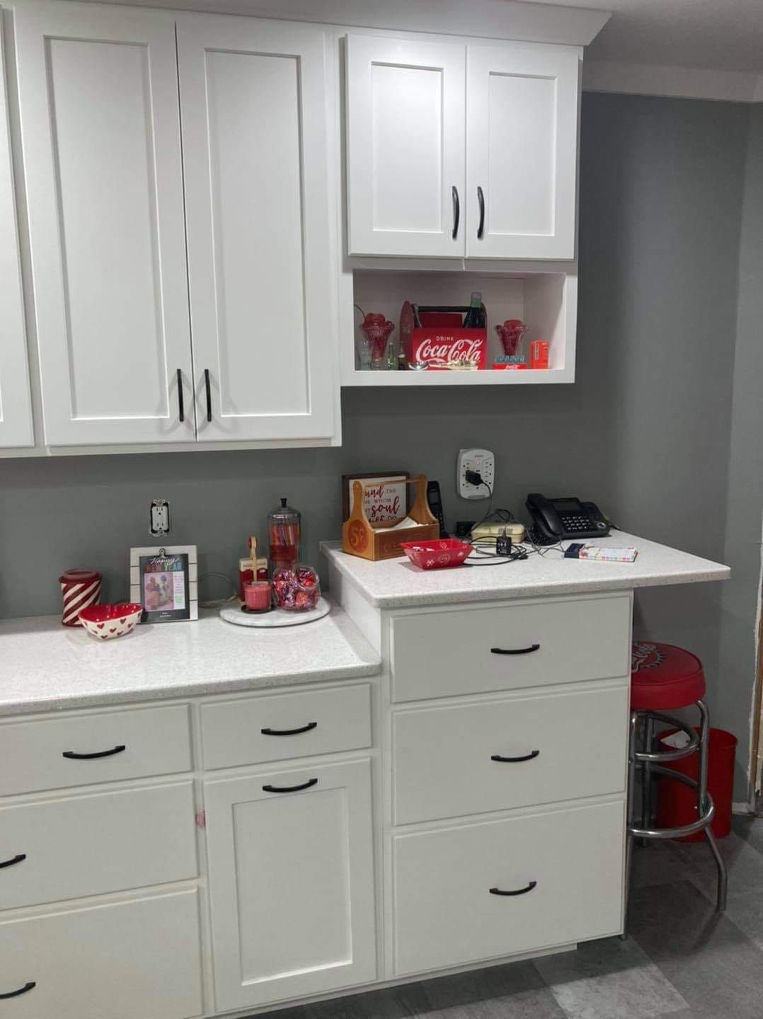 A kitchen with white cabinets and drawers and a red chair.
