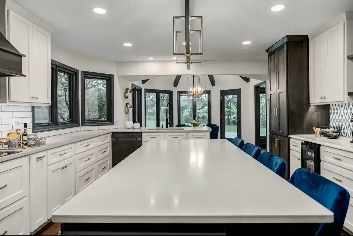 A kitchen with white cabinets and blue chairs and a long white table.