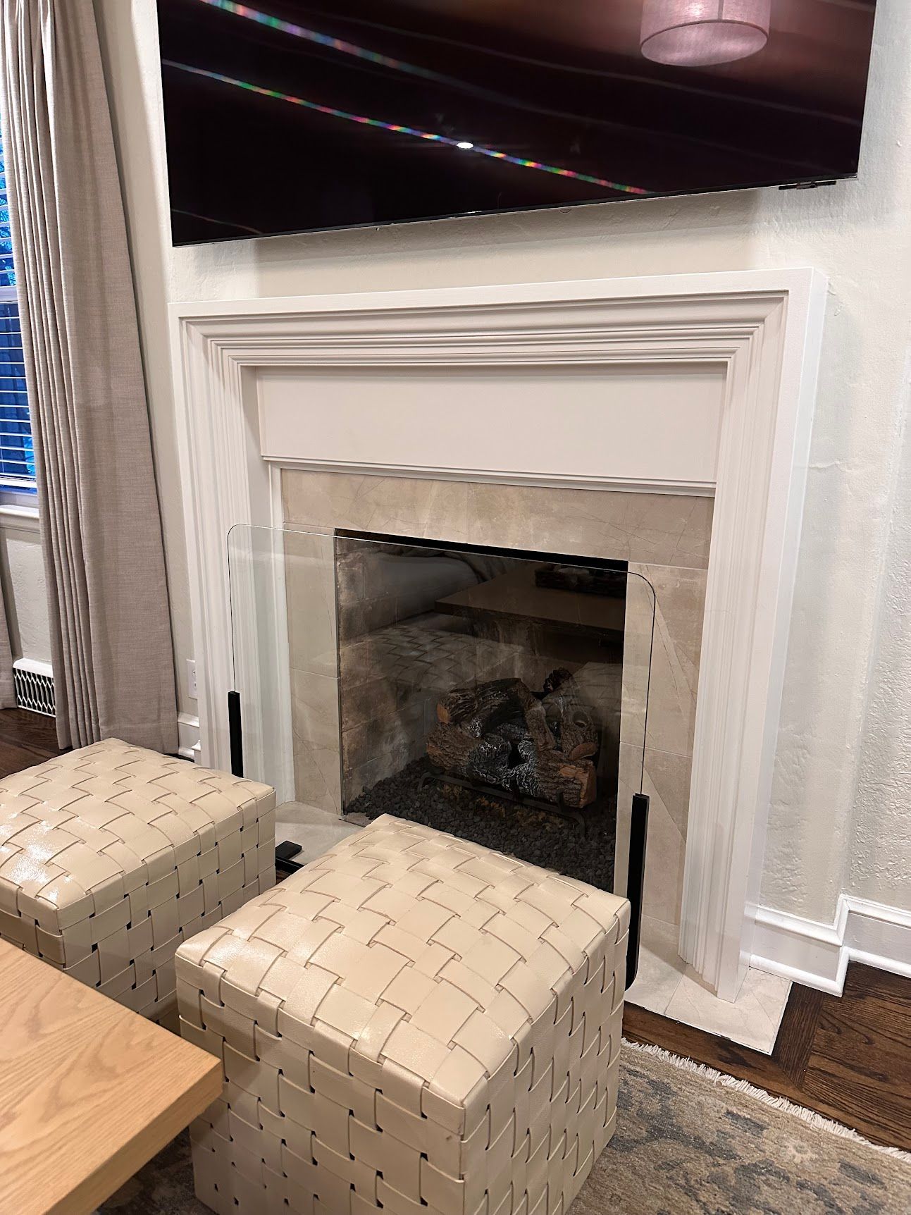 A living room with a fireplace , ottomans , and a flat screen tv.