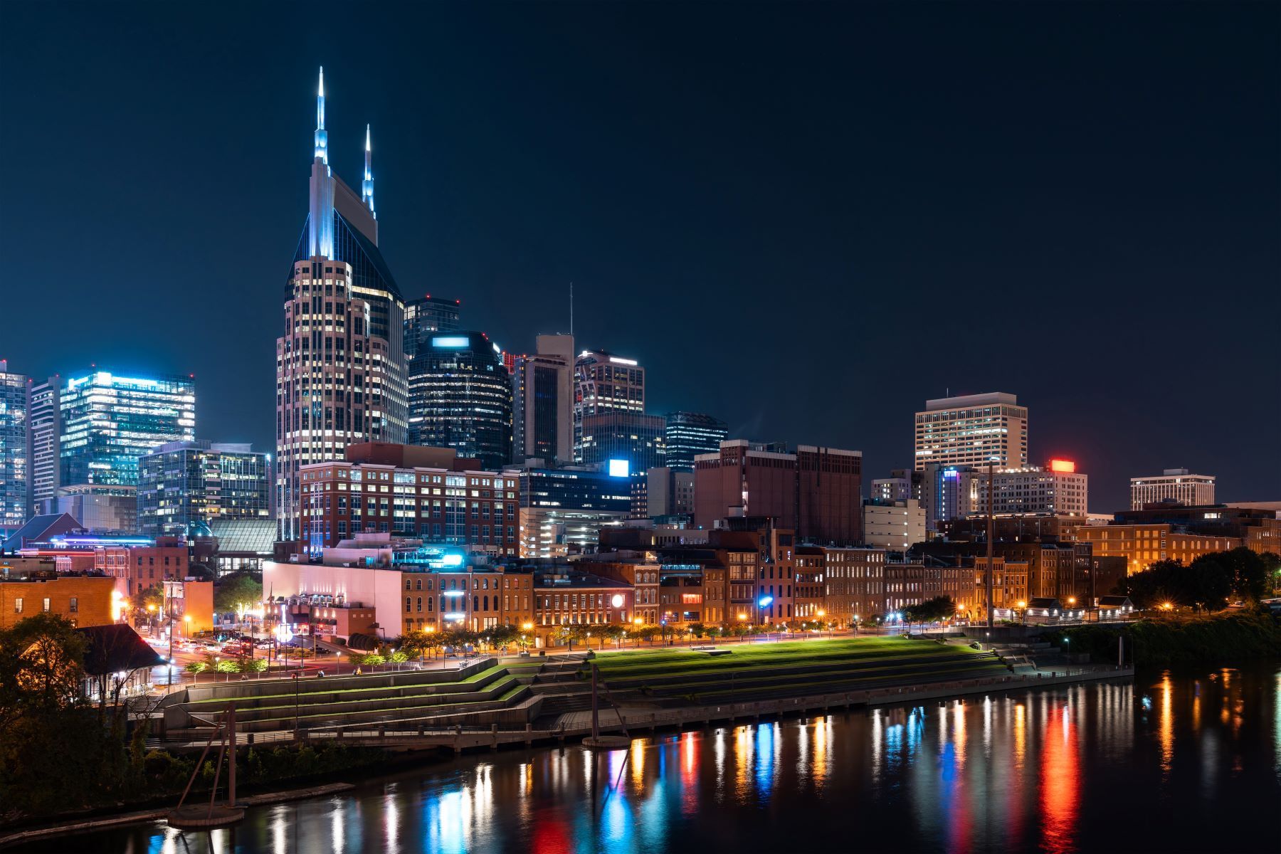 A city skyline at night with a river in the foreground.