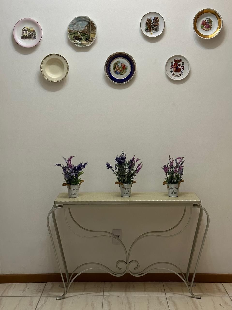 Uma mesa com três vasos de plantas e pratos na parede atrás dela