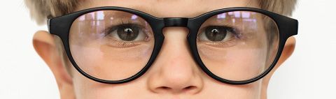 Primer plano del rostro de una persona con gafas negras de montura redonda. Se ven los ojos a través de las lentes.