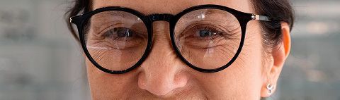 Primer plano de una persona con gafas negras redondas. Arrugas visibles alrededor de los ojos.