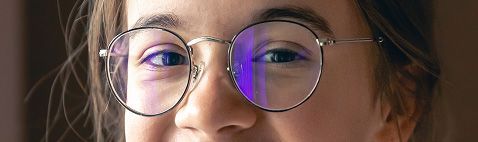 Primer plano del rostro de una persona con gafas redondas. Se ven reflejos en las lentes; los ojos están abiertos.