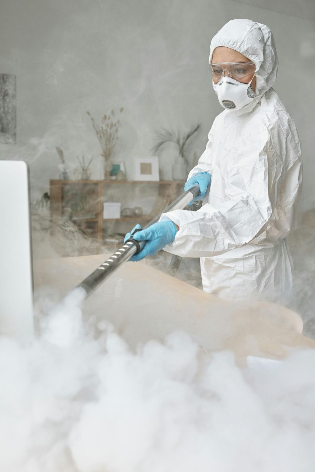A person wearing protective gear inspects a white cloth on a wooden table near a window.