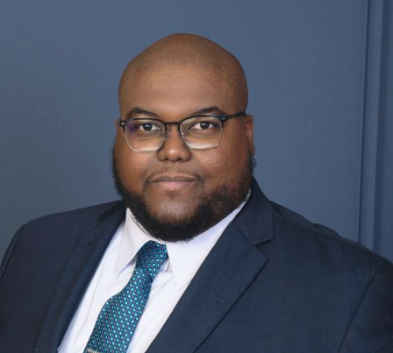 A bald man with glasses and a beard is wearing a suit and tie.