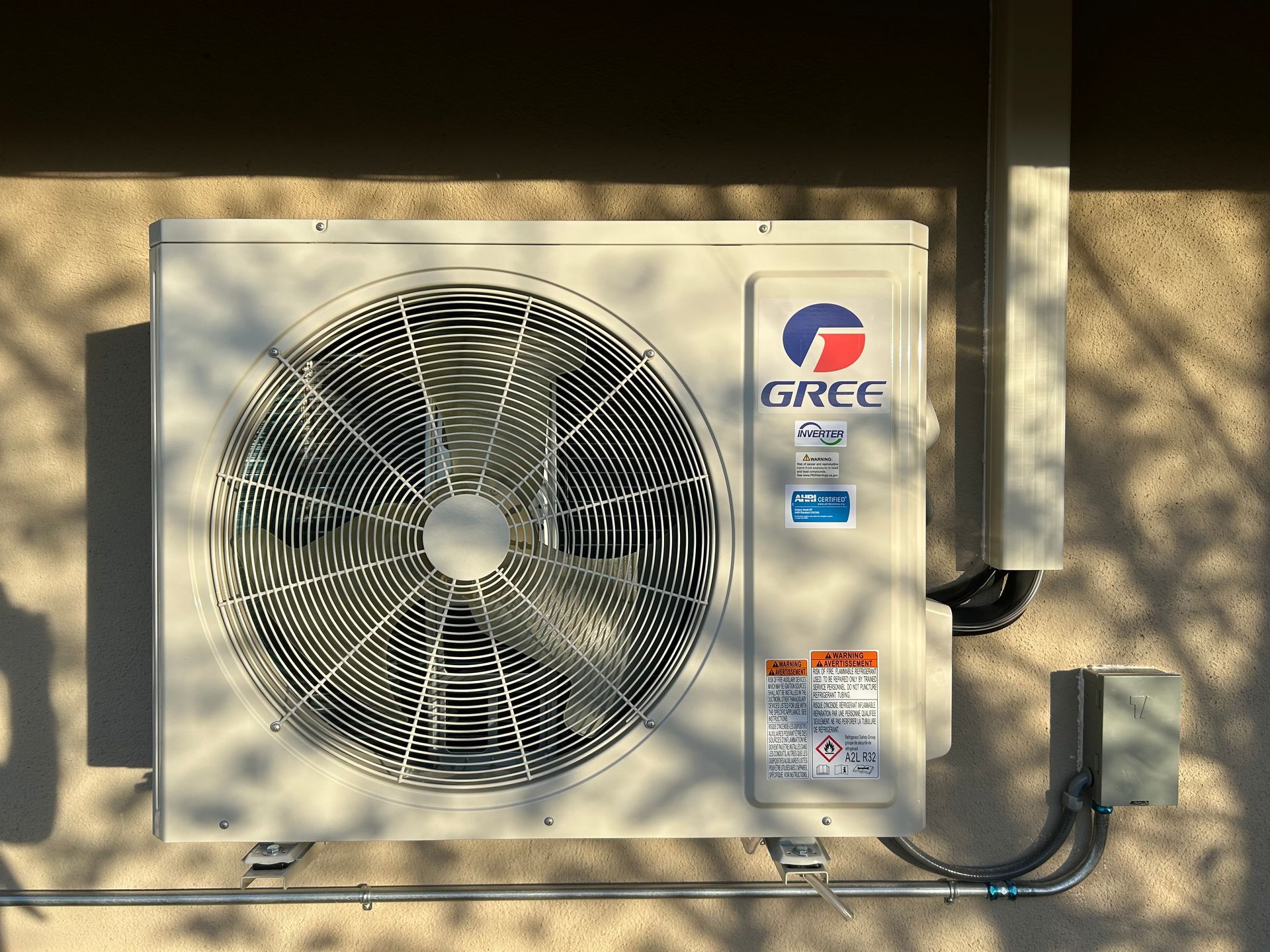 Gree air conditioner unit mounted on a beige building exterior with a sunlight shadow.