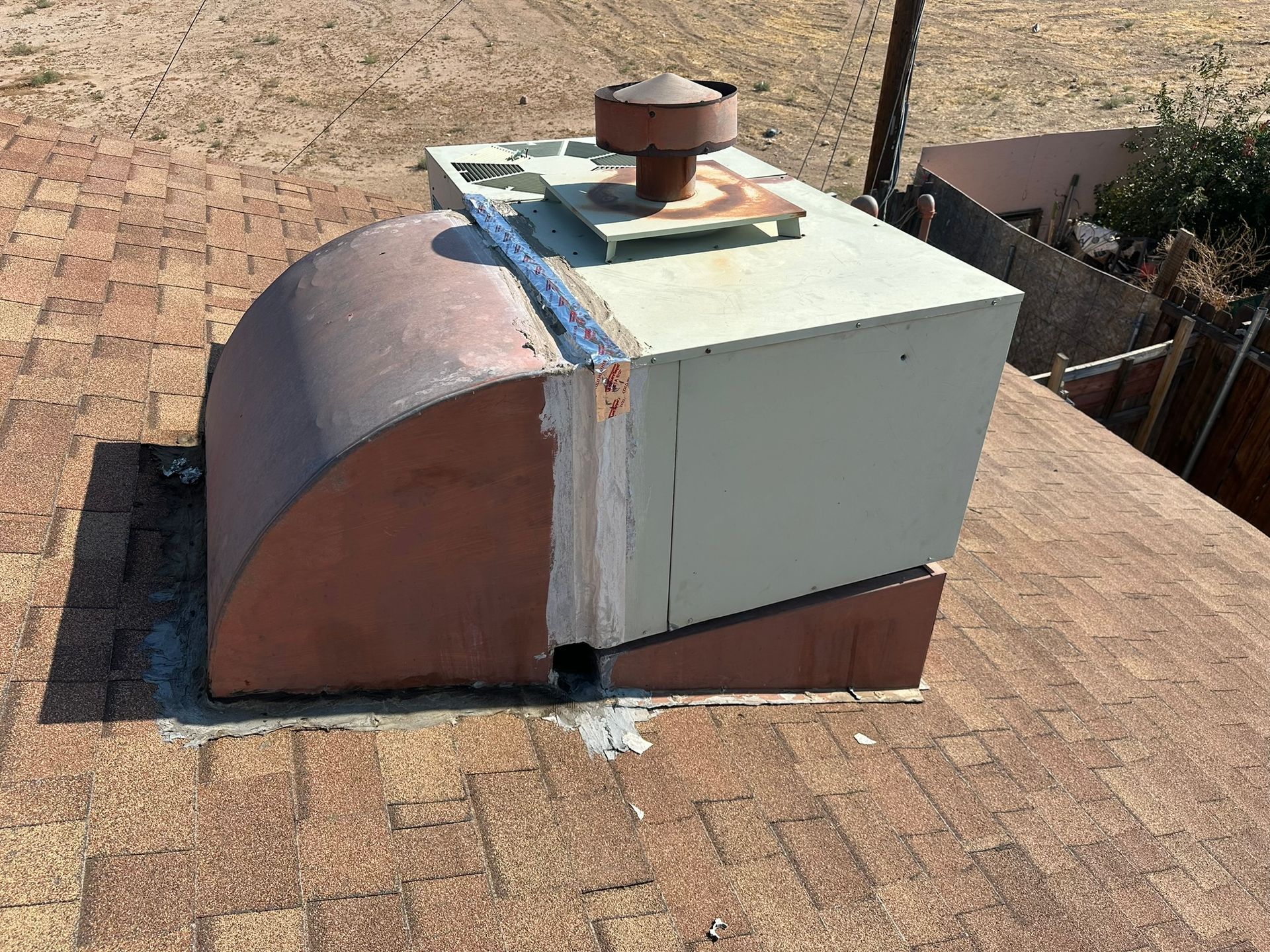 Metal HVAC unit on a brown shingle roof, with a rounded shield, and a rusty top.