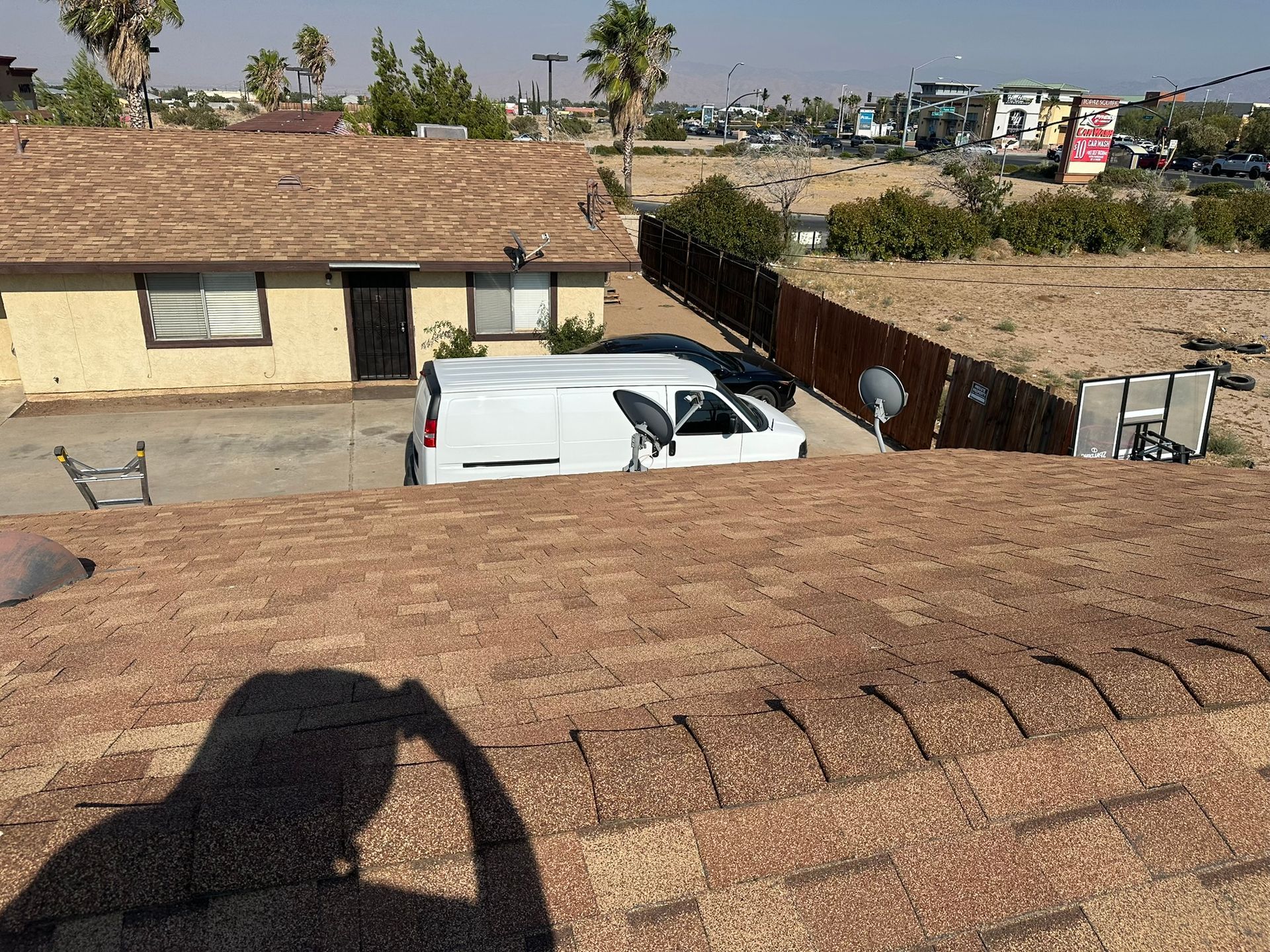 View from a roof, showing a white van parked near a house, with a fence and street in the distance.