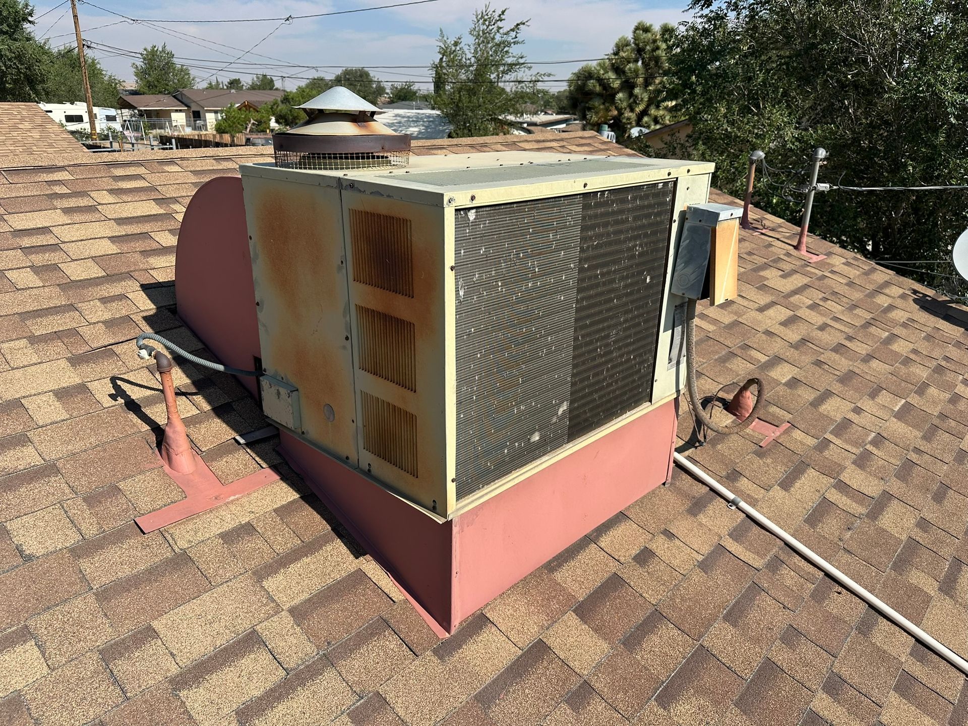 A weathered rooftop air conditioning unit on a brown shingle roof.