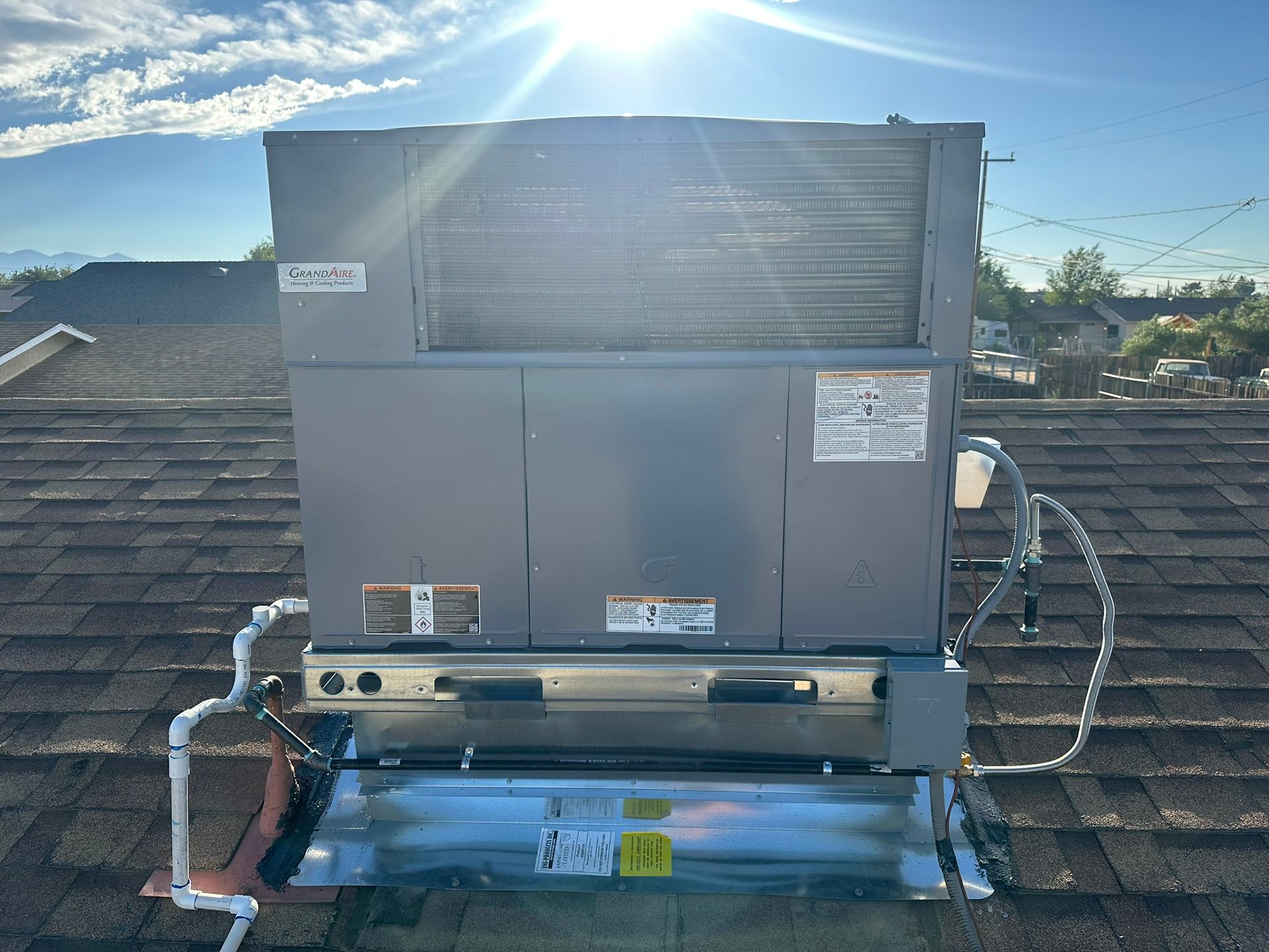 Rooftop HVAC unit, gray metal, installed on shingle roof under bright sunlight.