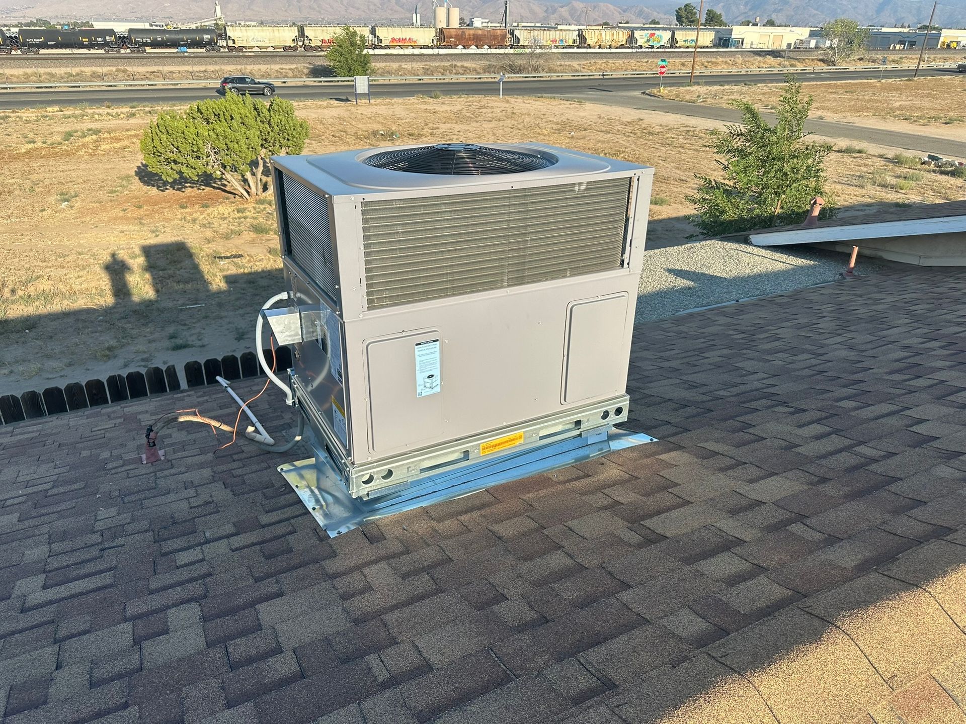 HVAC unit on a rooftop, set against a background of train tracks and dry landscape.