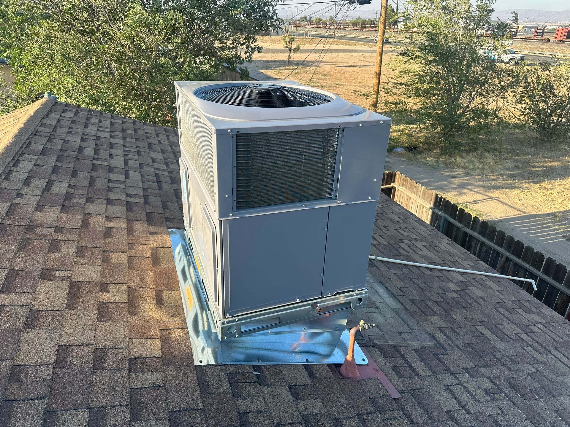 Gray air conditioning unit on a rooftop with a brown shingled roof, outdoors.