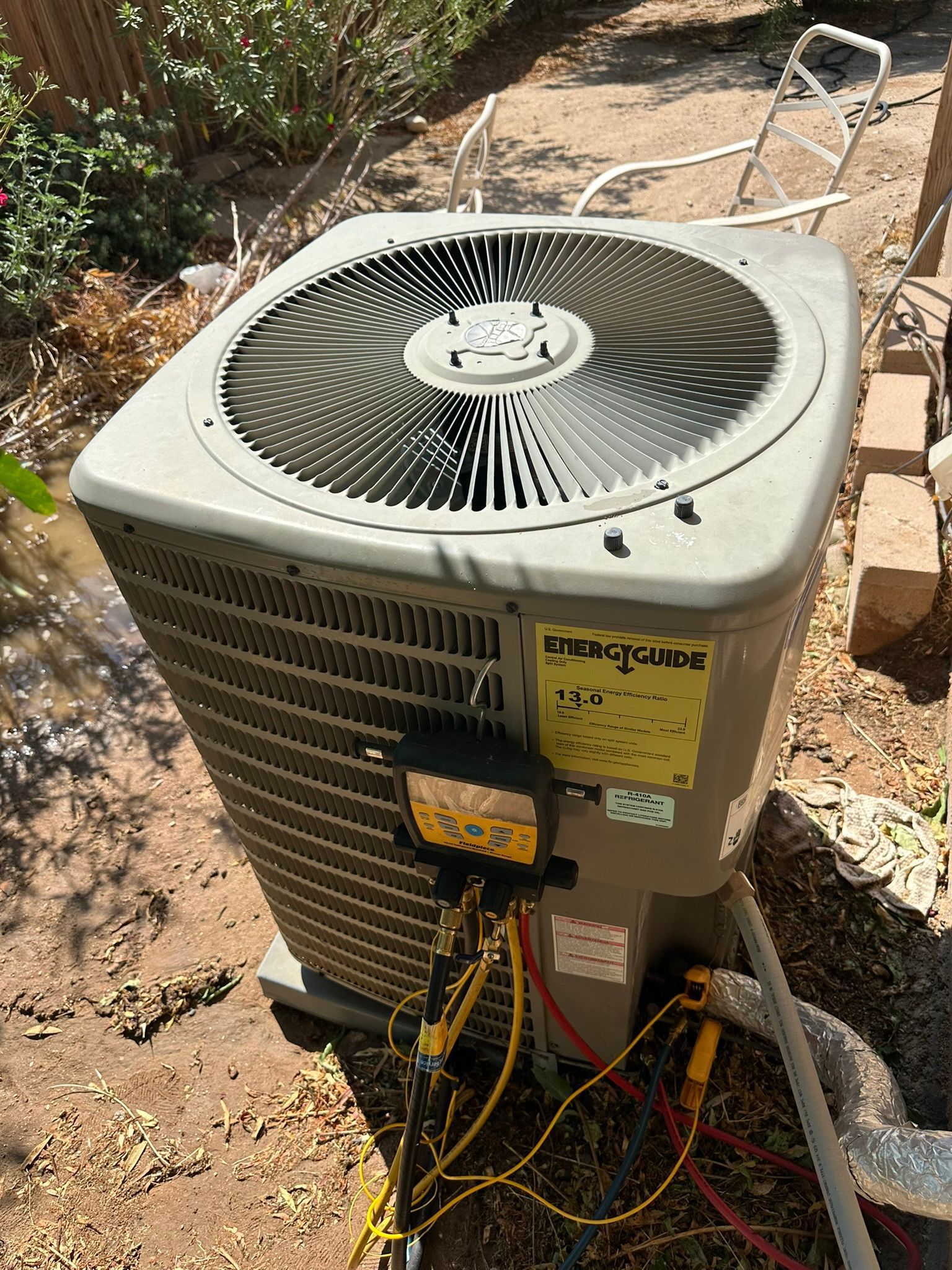 Outdoor air conditioning unit with gauges attached, in a yard.