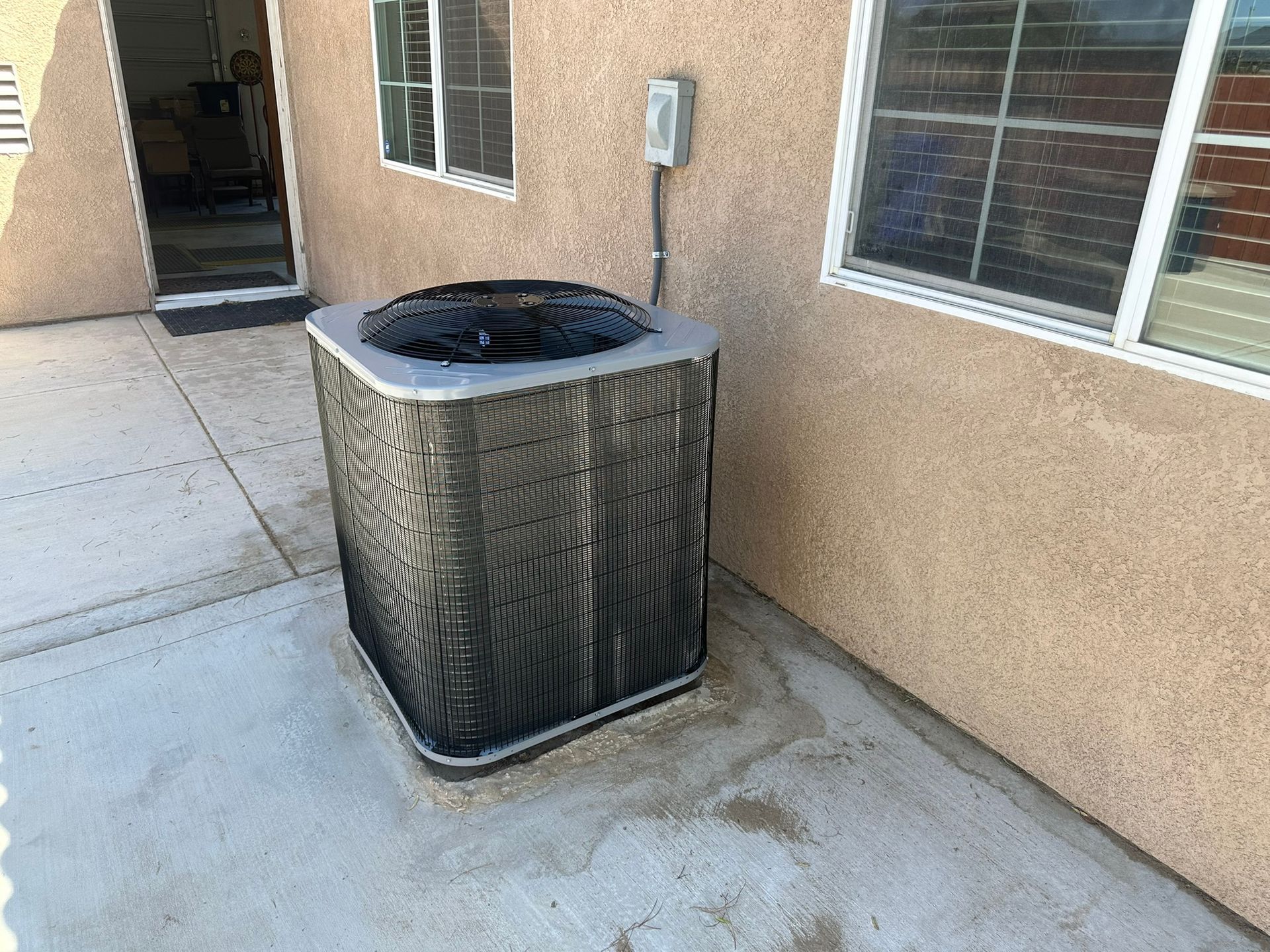 Air conditioner unit outside a building near a window. Beige stucco wall.
