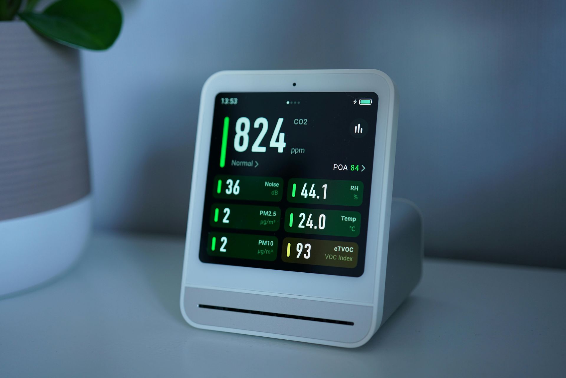 White air quality monitor displays real-time data with green and white text on a white nightstand.