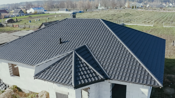 Close-up of a house roof with gray shingles, dark metal roof, and white trim with a gutter.