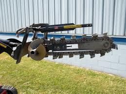 A trenching machine, black and silver, is mounted on a tractor, ready to dig.