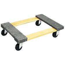 A wooden furniture dolly with gray carpeted ends and four black wheels.