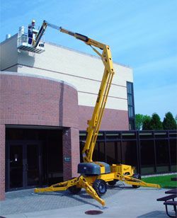 Yellow aerial lift with a worker near a building's roof. The lift is extended.