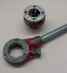 Red and silver pipe threader tool with a die head on a surface.