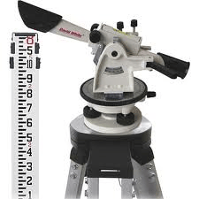 Surveyor's level on tripod with a measuring rod; white, gray, and black; outdoors, for measuring elevation.