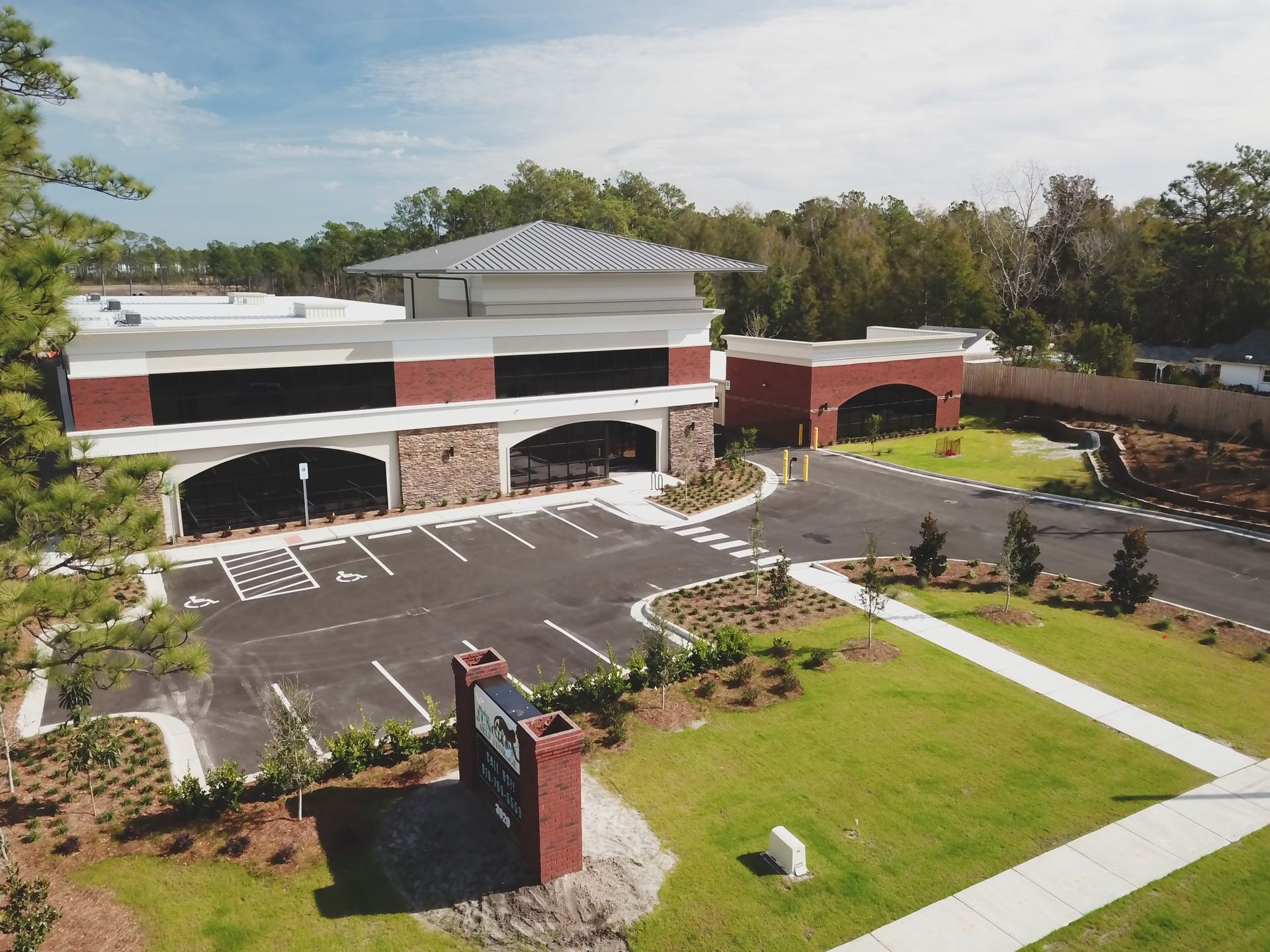 Office building with brick and stone facade, parking lot, and green lawn.