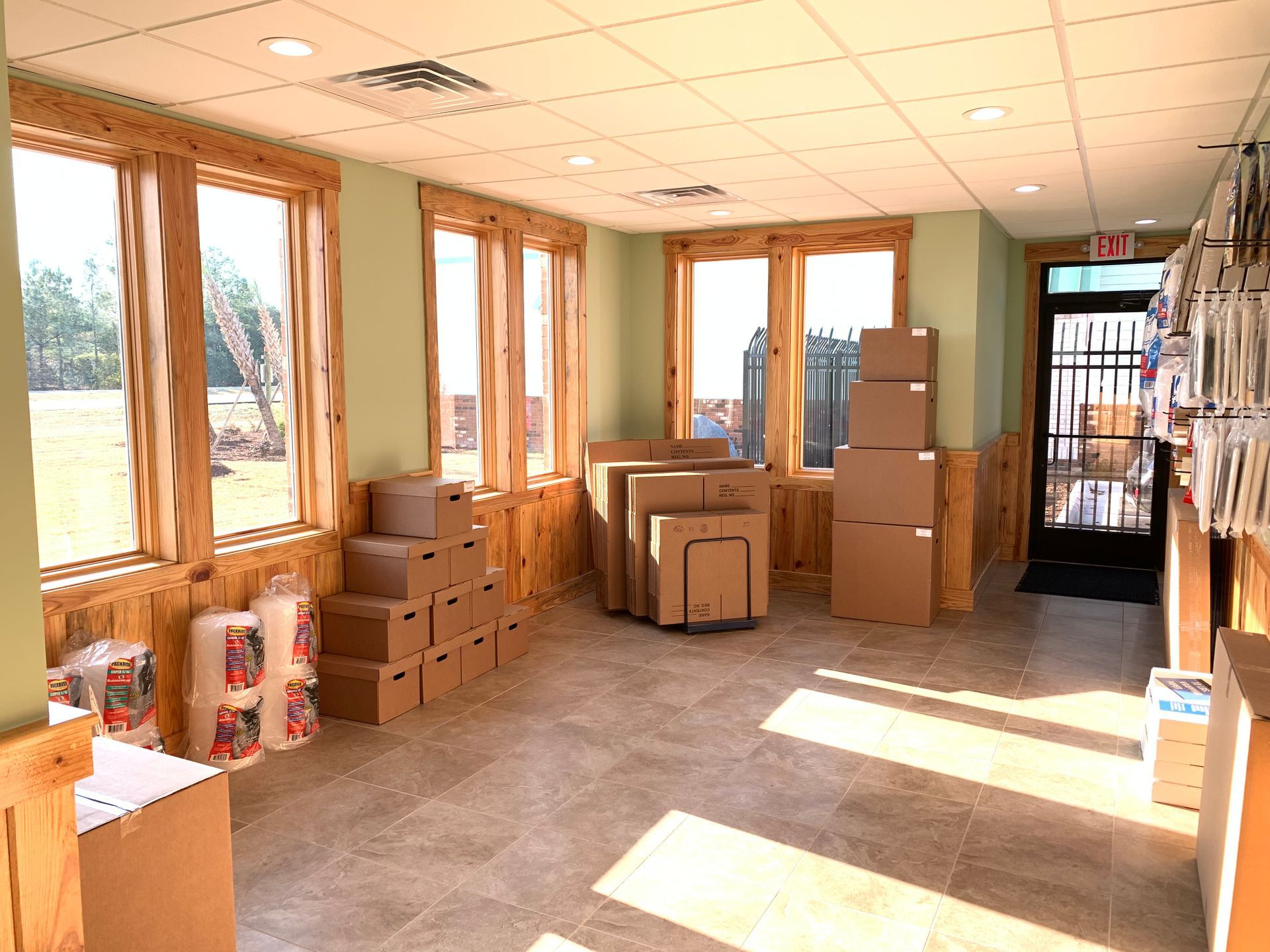 Empty store interior with wood trim, boxes, and sunlight streaming through windows.