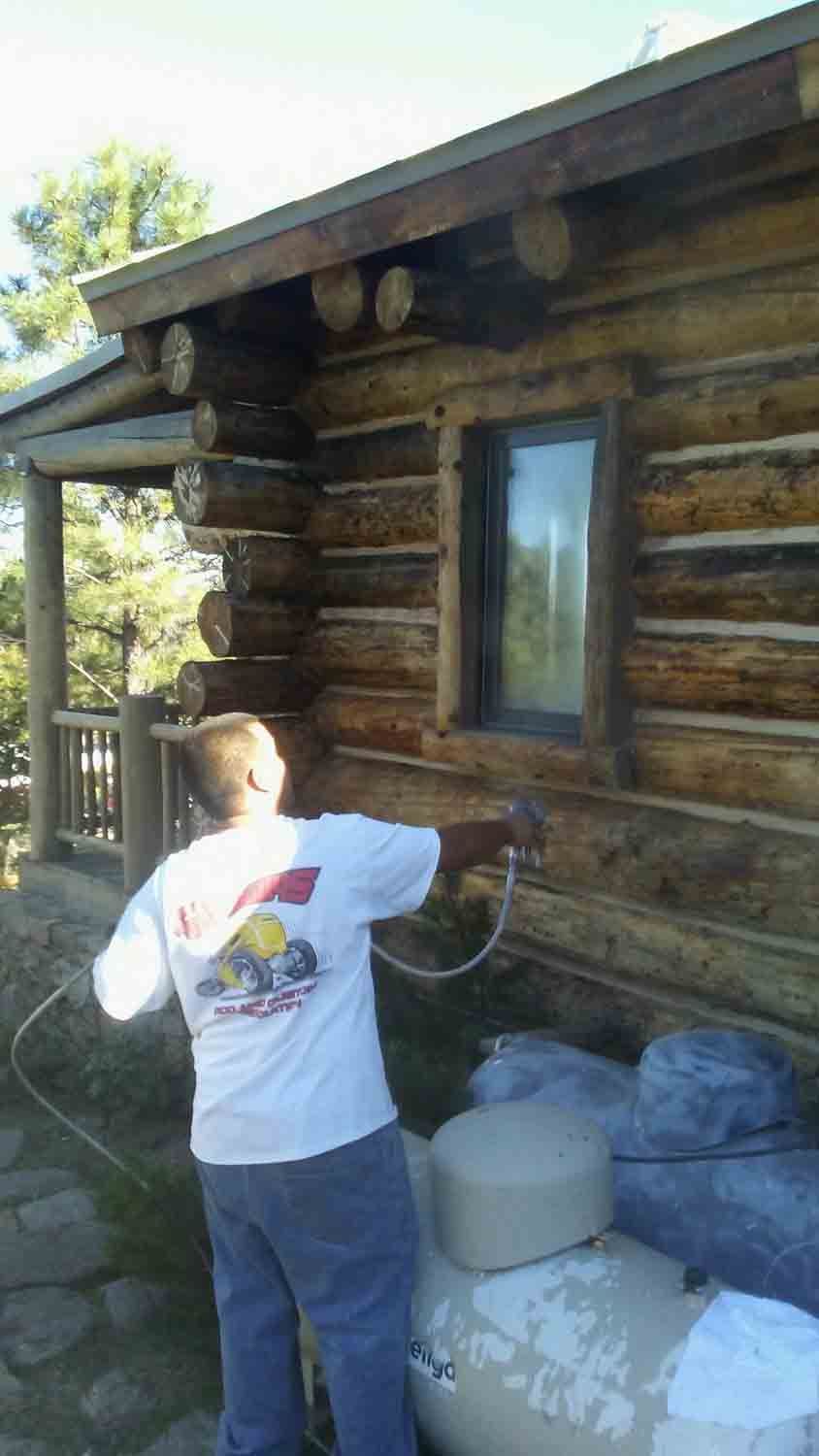 A man is spray painting the side of a log cabin.