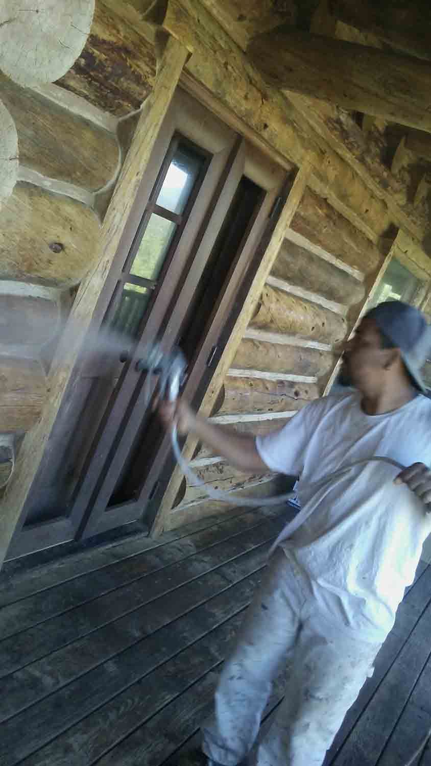 A man is spraying a door with a hose in front of a log cabin.