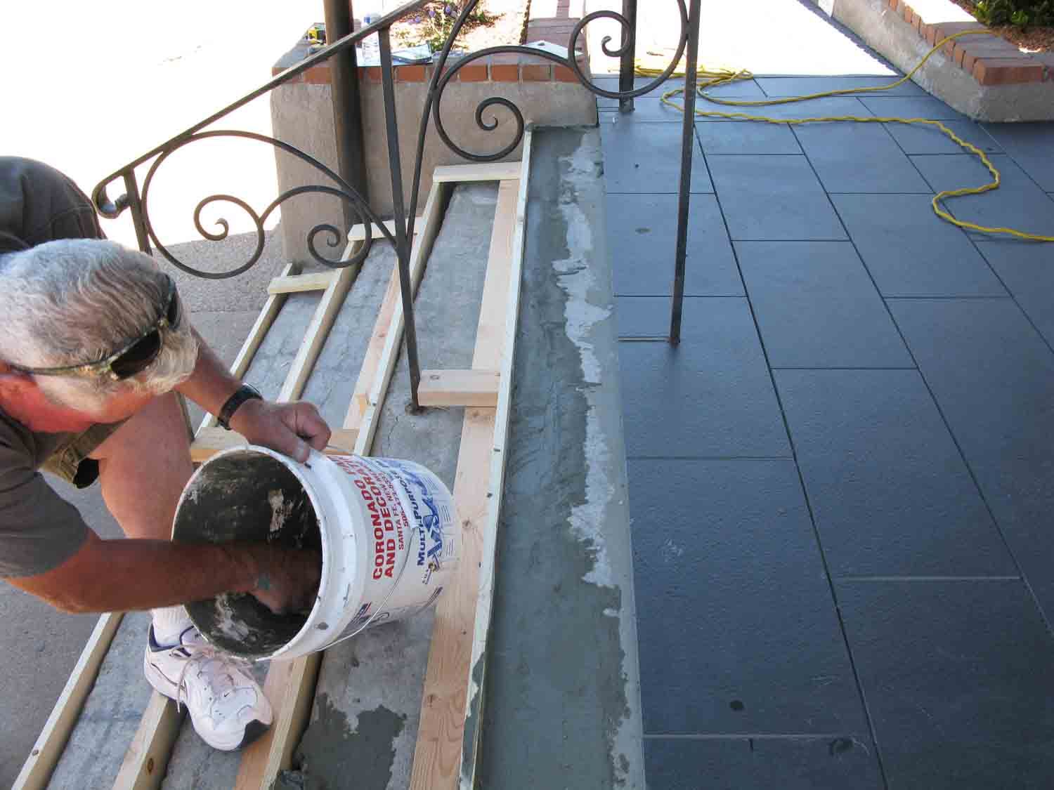 A man is pouring cement into a bucket that says ' concrete ' on it
