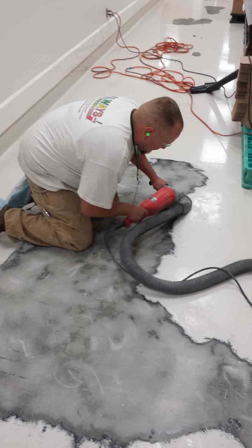 A man is kneeling on the floor using a vacuum cleaner.