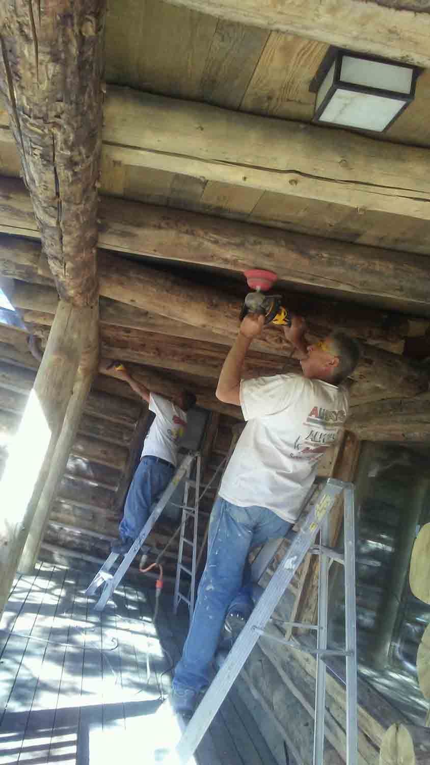 A group of men are working on the ceiling of a log cabin.