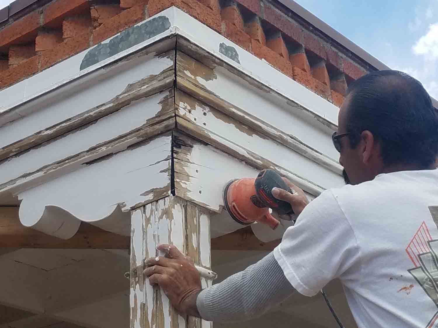 A man is sanding a piece of wood on a porch.