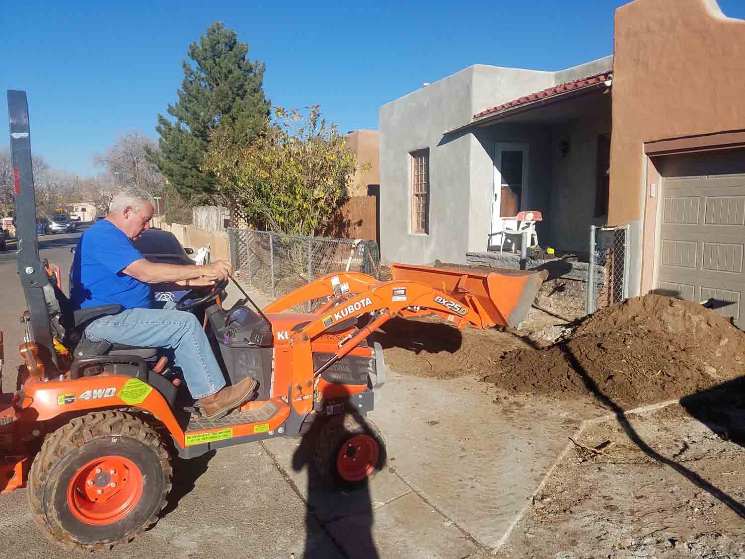 A man is driving an orange tractor in front of a house.