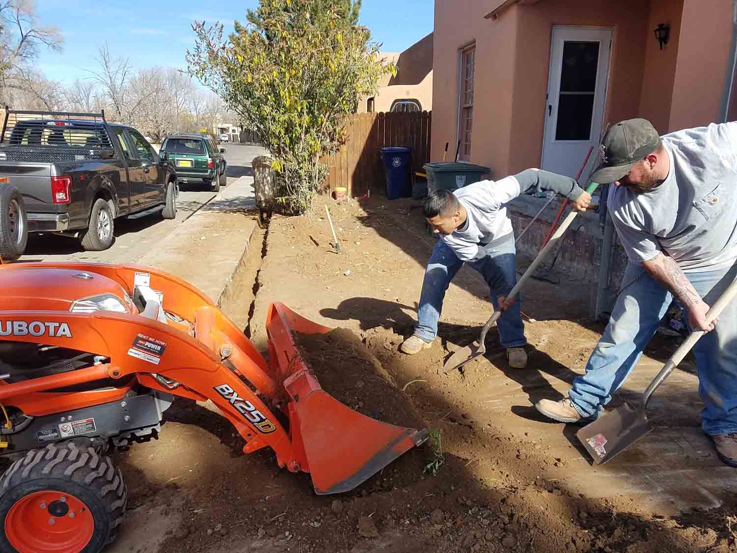 Two men are digging in the dirt next to a tractor.