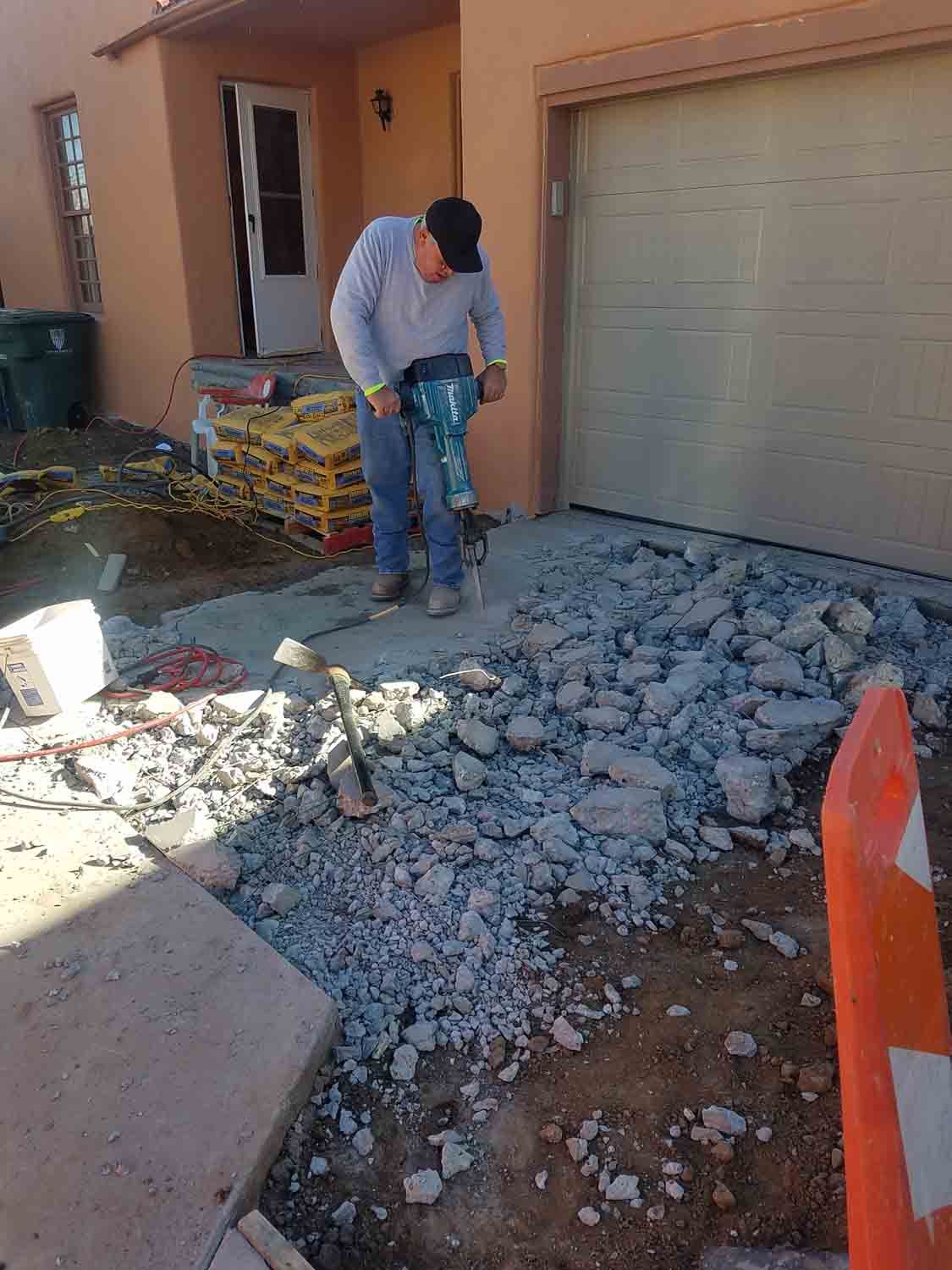 A man is using a hammer to break concrete in front of a garage.