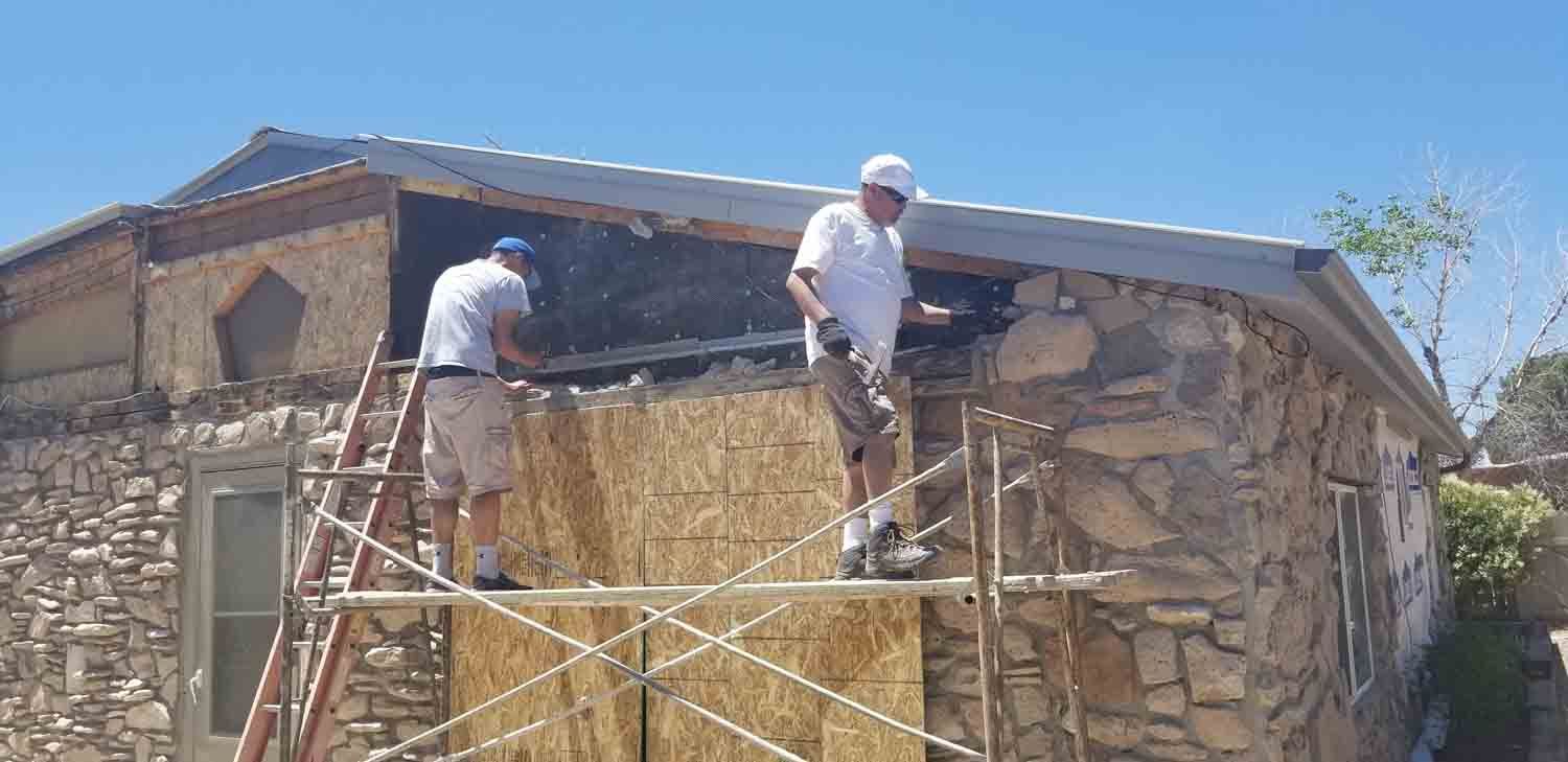 Two men are working on a stone building on a scaffolding.